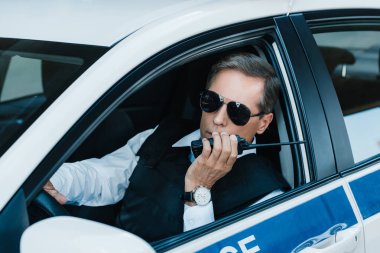 Orta yaşlı erkek polis memuru arabaya ayarla radyo konuşurken güneş gözlüğü 