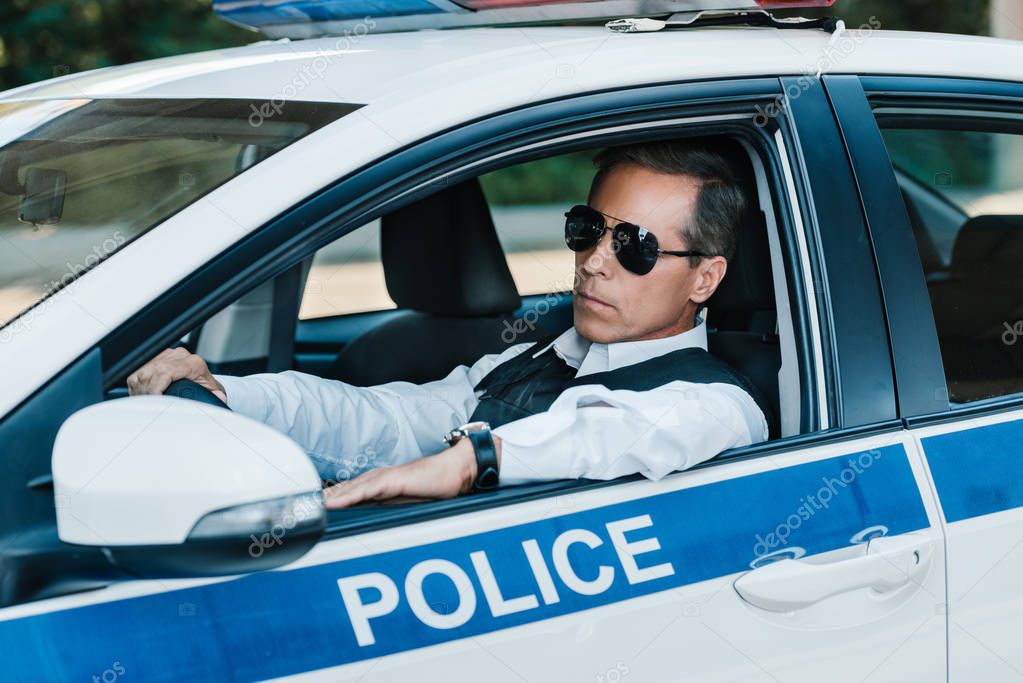 confident mature policeman in sunglasses sitting in car 