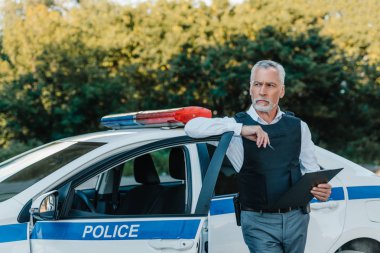 Orta yaşlı polis memuru Pano ile ayakta ve uzak araba Sokağı'nda seyir kurşun geçirmez yelek