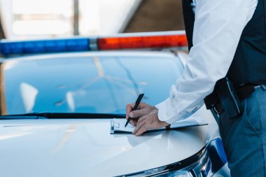 cropped image of male police officer writing in clipboard on car at street clipart