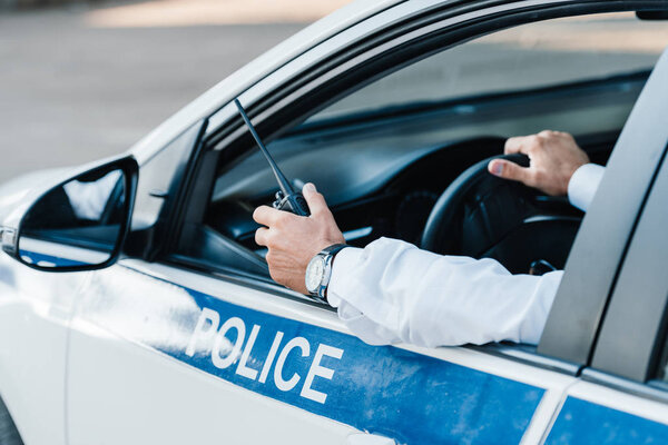 cropped image  of male police officer holding walkie-talkie in car 
