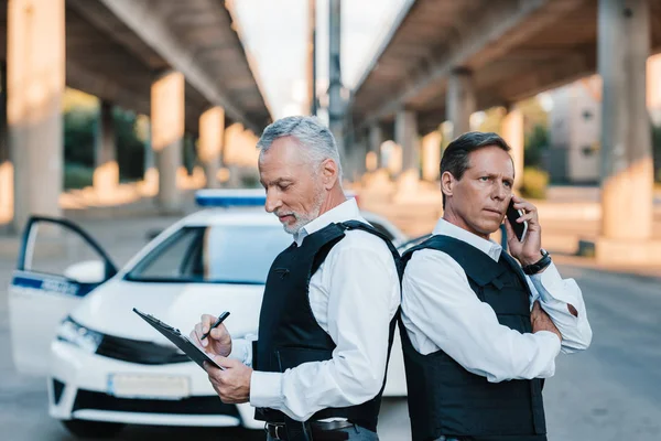 Mature Police Officer Talking Smartphone Standing Colleague Back Back While — Stock Photo, Image