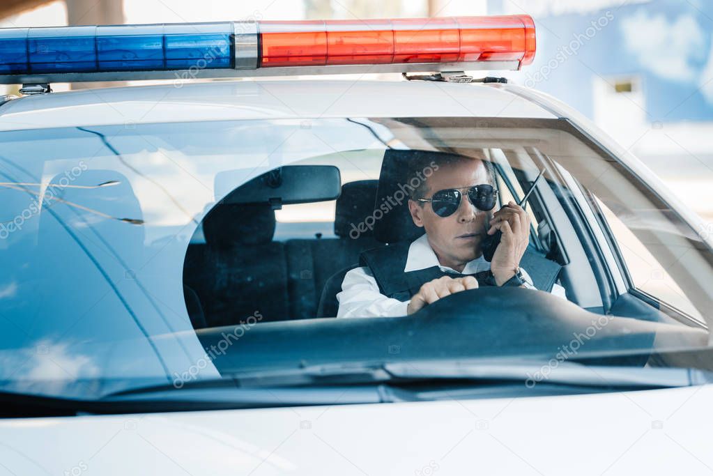 serious middle aged policeman in sunglasses talking on radio set in car 