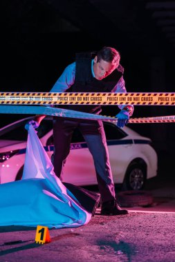 Orta yaşlı erkek polis olay yerinde ceset torbası içinde ceset bakarak memuru 