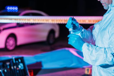 koruyucu elbise ve kanıt şişesi koyarak tarafından olay yerinde cımbız cesetle lateks eldiven erkek kriminoloji uzmanı kısmi görünümünü 