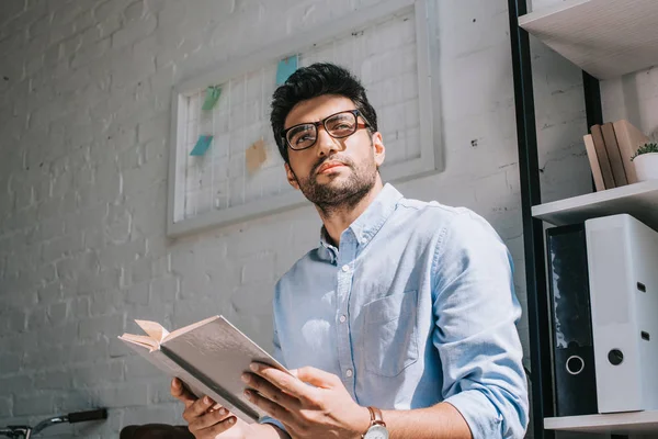 Guapo Arquitecto Gafas Sosteniendo Libro Mirando Hacia Otro Lado Oficina —  Fotos de Stock