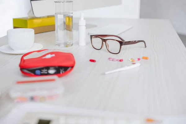 first aid kit, pills, glasses and glass of water on table in office