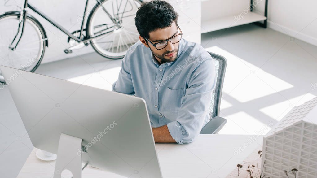 handsome architect using computer and looking at architecture model in office
