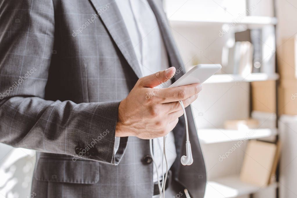 cropped image of businessman holding smartphone and earphones in office