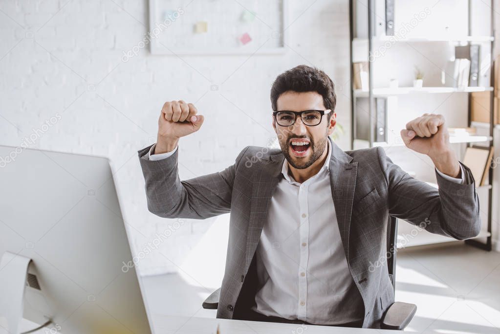 excited handsome businessman screaming and showing yes gesture in office