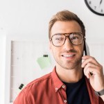 Smiling businessman in glasses talking on smartphone in office