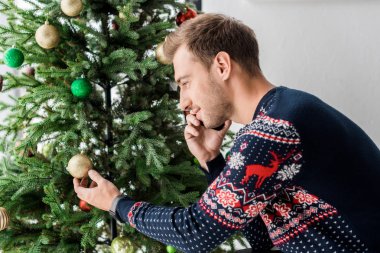 smartphone üzerinde konuşmak ve Noel ağacı oyuncak dokunmadan Noel kazaklı adam