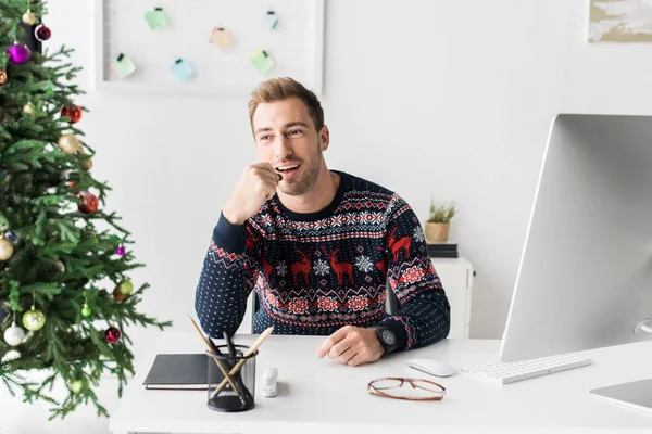 近代的なオフィスのテーブルに座ってクリスマス セーターのビジネスマン — ストック写真