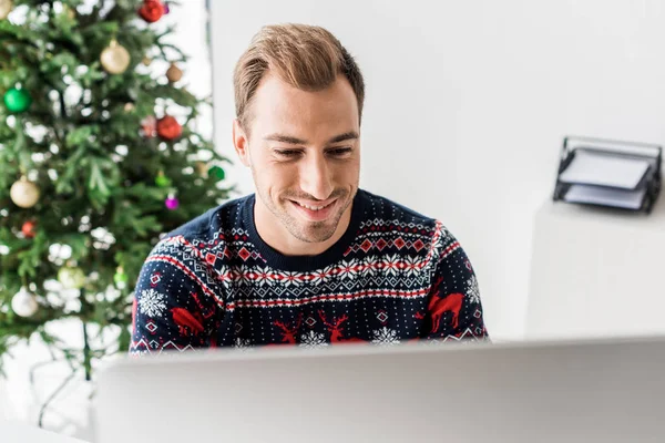 近代的なオフィスのコンピューターを使用してクリスマスのセーターのビジネスマン  — 無料ストックフォト
