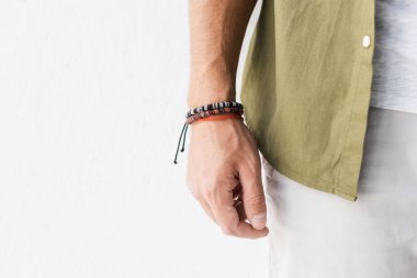 cropped view of male hand with bracelets against white wall