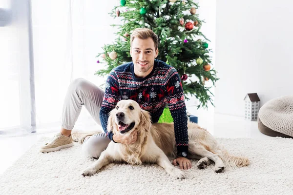 happy man in sweater with golden retriever dog sitting near christmas tree