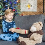 Adorable child in pajamas holding christmas gift and looking at teddy bear