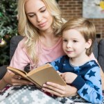 Mooie jonge moeder en schattige lachende zoon lezen boek samen bij Kersttijd