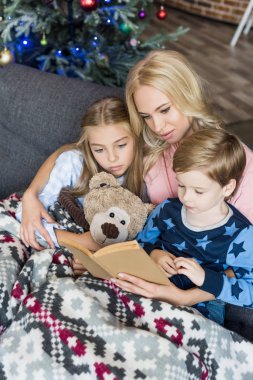 high angle view of young mother reading book with cute children in pajamas at christmas time  clipart