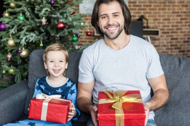 mutlu baba ve sevimli küçük oğlu Noel hediyeleri tutarak ve kameraya gülümseyen pijama