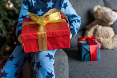 çocuğun kanepede oturan ve Noel hediyesi tutan pijama kırpılmış atış
