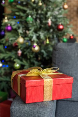 Kırmızı hediye kutusu üzerinde altın yay ile yakından görmek kanepe ve Noel ağacın arkasında dekore edilmiş 