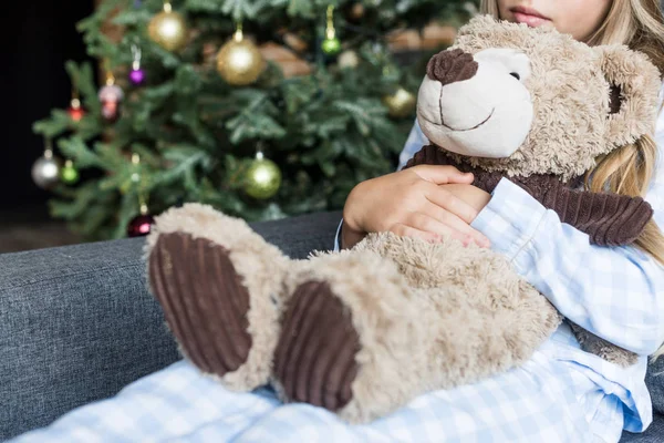 クマのぬいぐるみを抱いて クリスマスの時にソファーに座っていた子供のショットをトリミング — ストック写真
