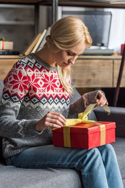 家庭でクリスマス プレゼントを開く美しい若いブロンドの女性  — 無料ストックフォト