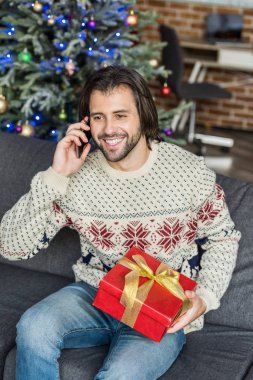 Noel hediyesi tutarak ve smartphone ile konuşurken yakışıklı mutlu adamın yüksek açılı görünüş
