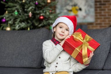 Noel hediyesi tutarak ve kameraya bakarak santa şapkalı şirin küçük çocuk