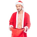 Leende muskulös man i santa claus kostym med jul-säck isolerad på vit bakgrund