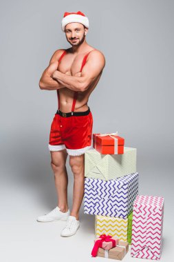 seksi kas santa Noel şapka ve hediye kutuları gri arka plan üzerine yığını yakınındaki Çapraz kollar ile ayakta şort