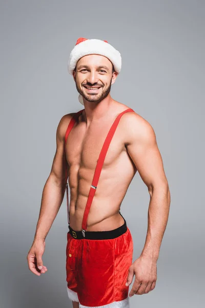 微笑的肌肉男人在圣诞帽看着相机孤立的灰色背景 — 免费的图库照片