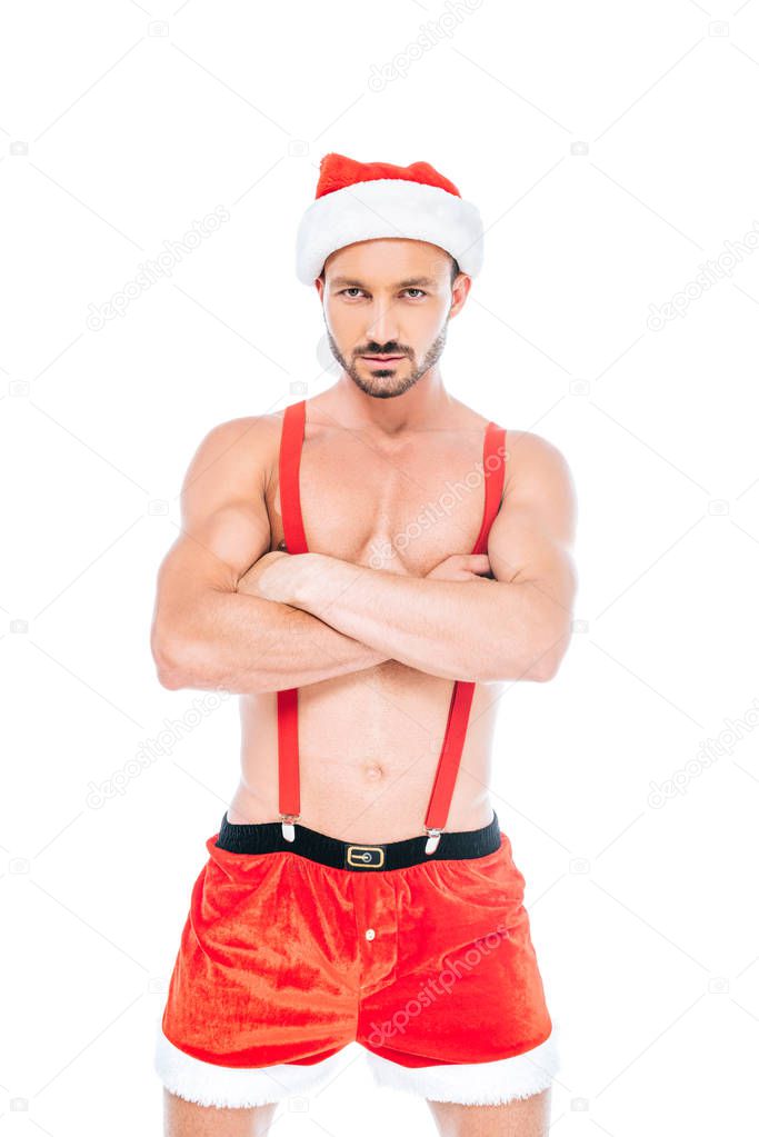 confident shirtless muscular man in christmas hat and shorts standing with crossed arms isolated on white background