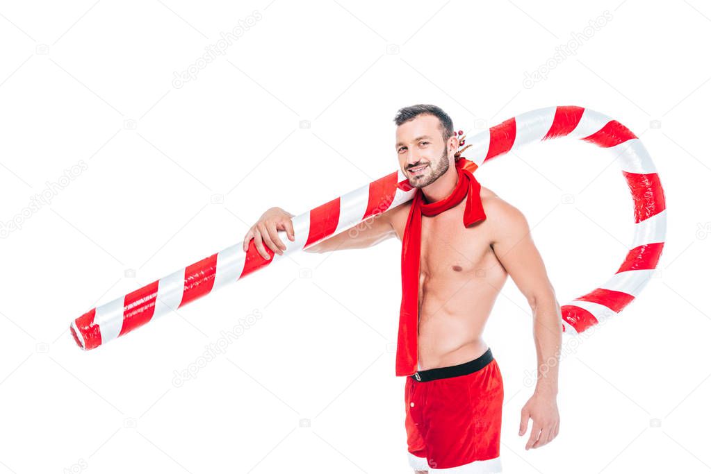 happy shirtless muscular man in santa shorts and red scarf holding striped christmas stick isolated on white background