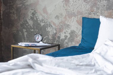 messy bed in loft bedroom with vintage alarm clock and newspaper on bedside table clipart