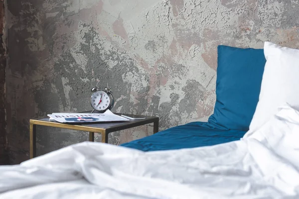 ビンテージの目覚まし時計やベッドサイド テーブルの上の新聞をロフト寝室の乱雑なベッド — ストック写真