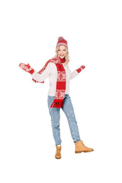 full length view of happy young woman in red hat, scarf and mittens smiling at camera isolated on white