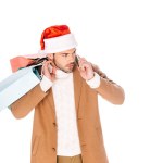 Young man in santa hat holding shopping bags and talking by smartphone isolated on white