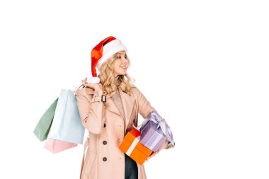 Noel Baba şapkası holding alışveriş torbaları ve üzerinde beyaz izole hediye kutuları gülümseyen genç kadında güzel 
