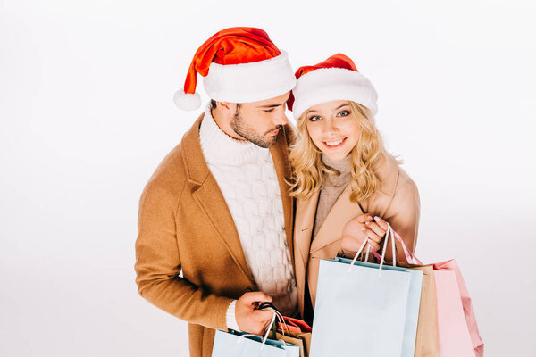 high angle view of beautiful happy young couple in santa hats holding shopping bags isolated on white