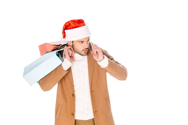 買い物袋を押し話を白で隔離のスマート フォンでサンタ帽子の若い男  — 無料ストックフォト