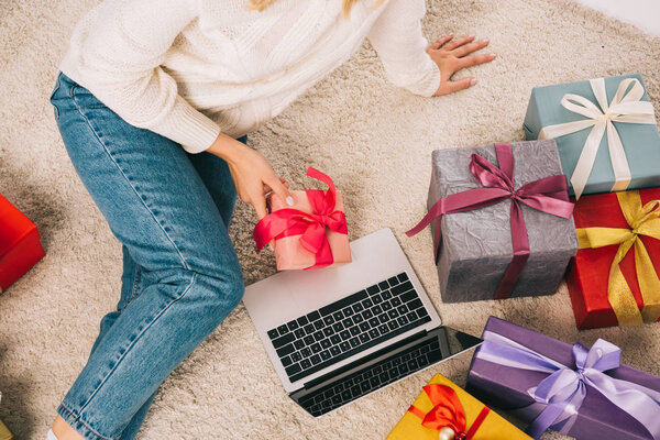 cropped shot of young woman holding christmas present and using laptop