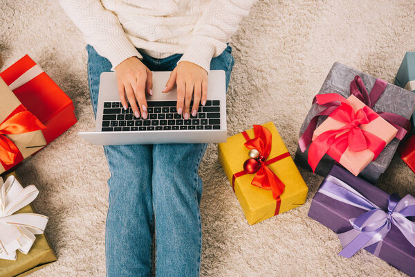 обрезанный снимок молодой женщины с помощью ноутбука, сидя возле рождественских подарков
