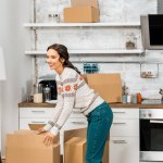 Attraktive junge Frau steht neben Pappkartons in Küche im neuen Zuhause