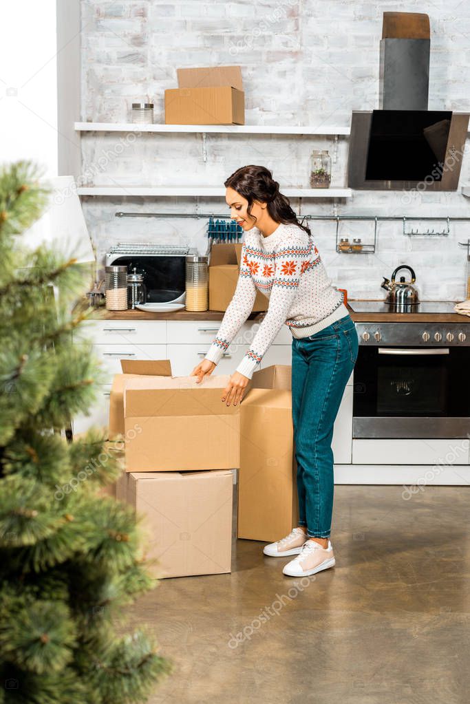 selective focus of woman standing near cardboard boxes in kitchen with christmas tree during relocation at new home 