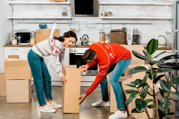 serious young couple carrying cardboard boxes for relocation in new home
