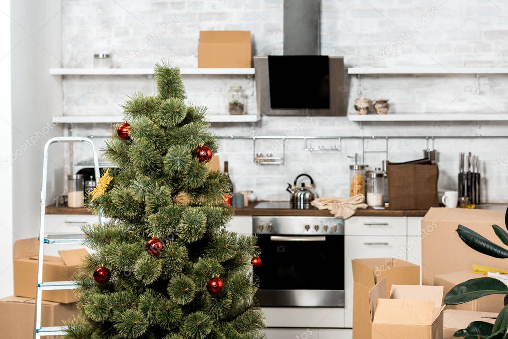 interior of kitchen with decorated christmas tree and cardboard boxes during relocation at new home 