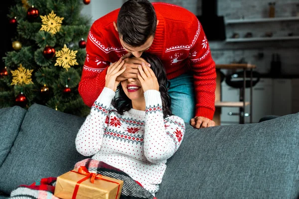 Junger Mann Schließt Augen Und Überrascht Lächelnde Freundin Auf Sofa — Stockfoto