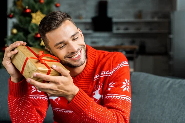 Felice Giovane Uomo Ascoltando Scatola Regalo Natale Sul Divano Casa — Foto stock gratuita